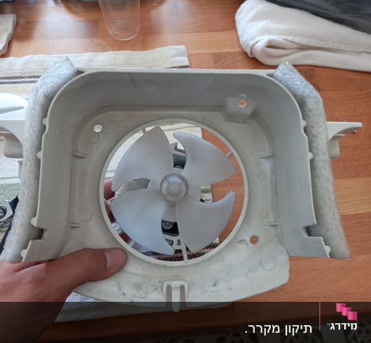 מאוורר פלסטיק לבן של מקרר מוחזק ביד על שולחן